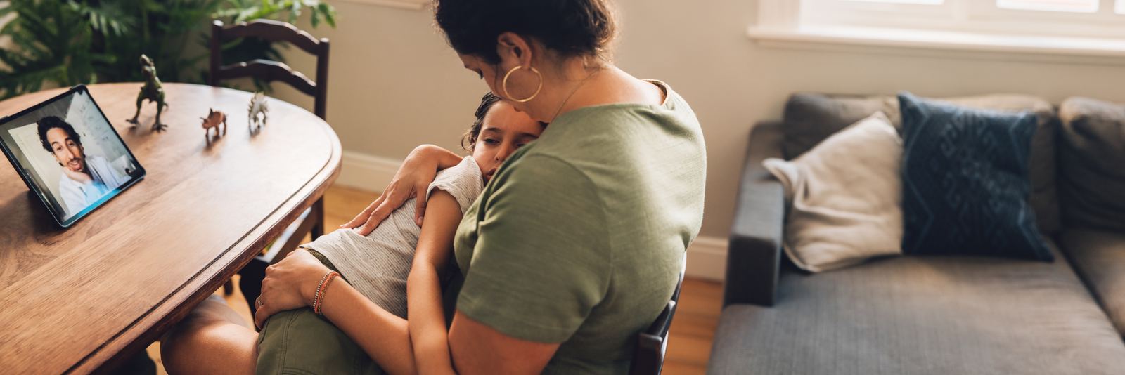A mother holding her child during a video visit with a doctor on a tablet